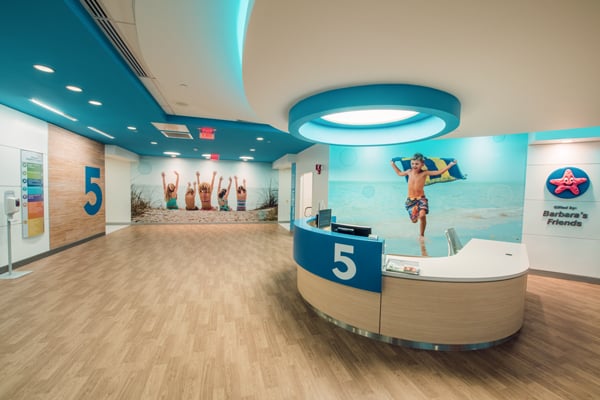 This hotel or resort lobby exhibits shades of blue and other colors that may appear on a beach and wall art of people on a beach.