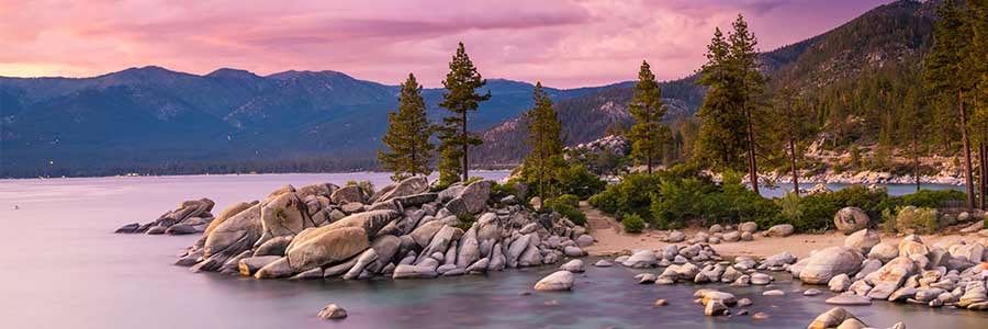 Image of a outcropping of rocks surrounded by water and mountains. 