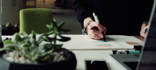 An Inpro interior designer standing at a desk with botanicals and other misc. items as the designer makes notes and sketches color schemes. 