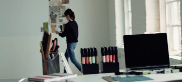 A creative desk with art tools, supplies, and a laptop, with designer Aga Artka in the background.