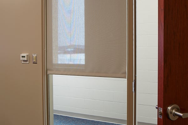 A brown window shade hanging in a window between a door and a wall.