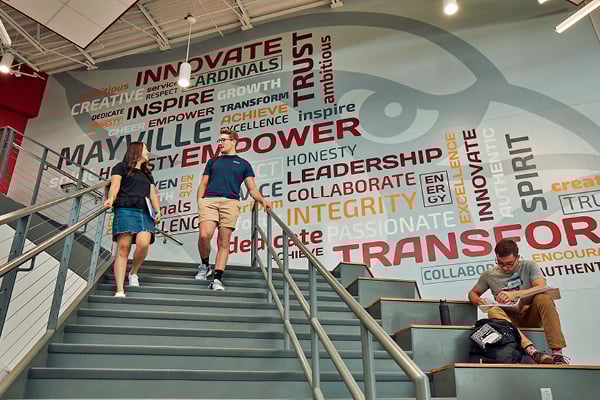 Students walking down stairs at school with a large scale word art mural behind them.