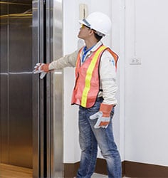 Man in a hardhat holding open a elevator with one arm