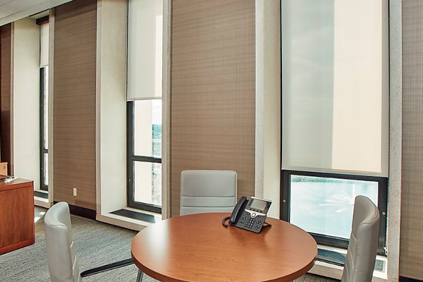 Office space with large windows from the ceiling to the floor with Inpro roller shades shown decreasing or increasing the light entering the room.