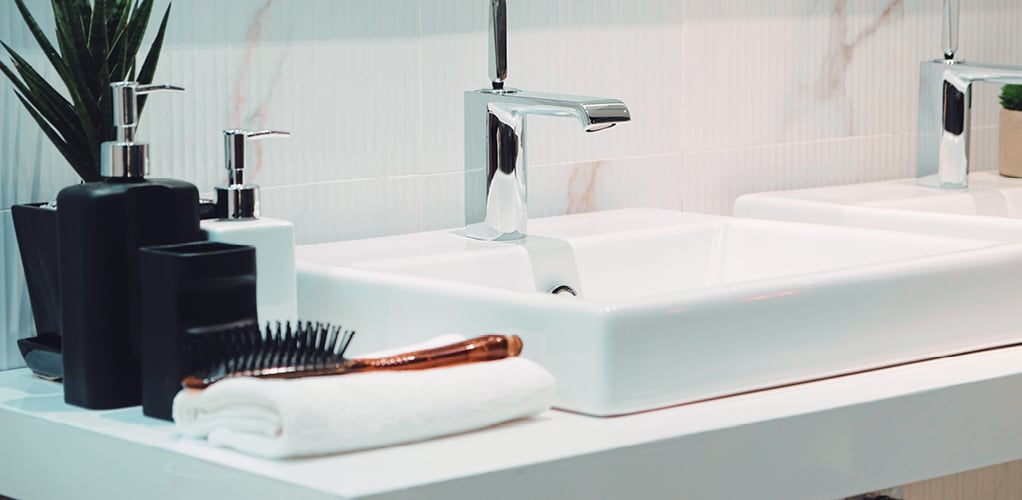 Raised white sink with several  pump containers and a hairbrush. 