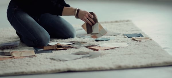 A woman, Aga Artka, from the shoulders down shown kneeling on a floor organizing Inpro color swatches and materials to create the 2020 Inpro Design Collection. 