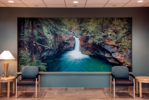A healthcare waiting room displaying biophilic designs through a large Inpro wall art of a waterfall in the forest. 