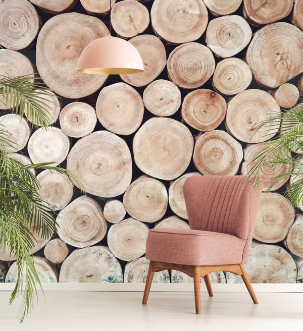 Lobby or office using biophilic design displaying the entire wall of tree trunk ends. A chair, hanging light, and green plants are also displayed.