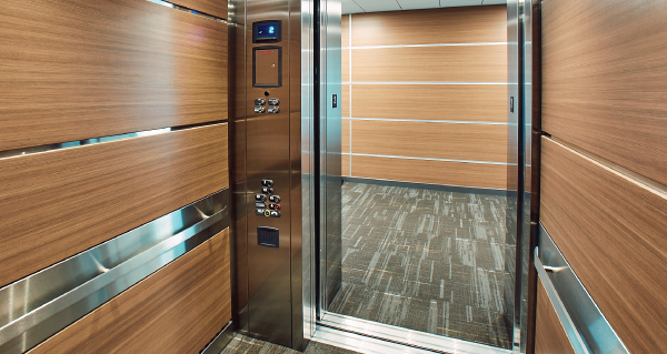 View of a hallway from the interior of an elevator cab with stainless steel handrails and woodland interior panels